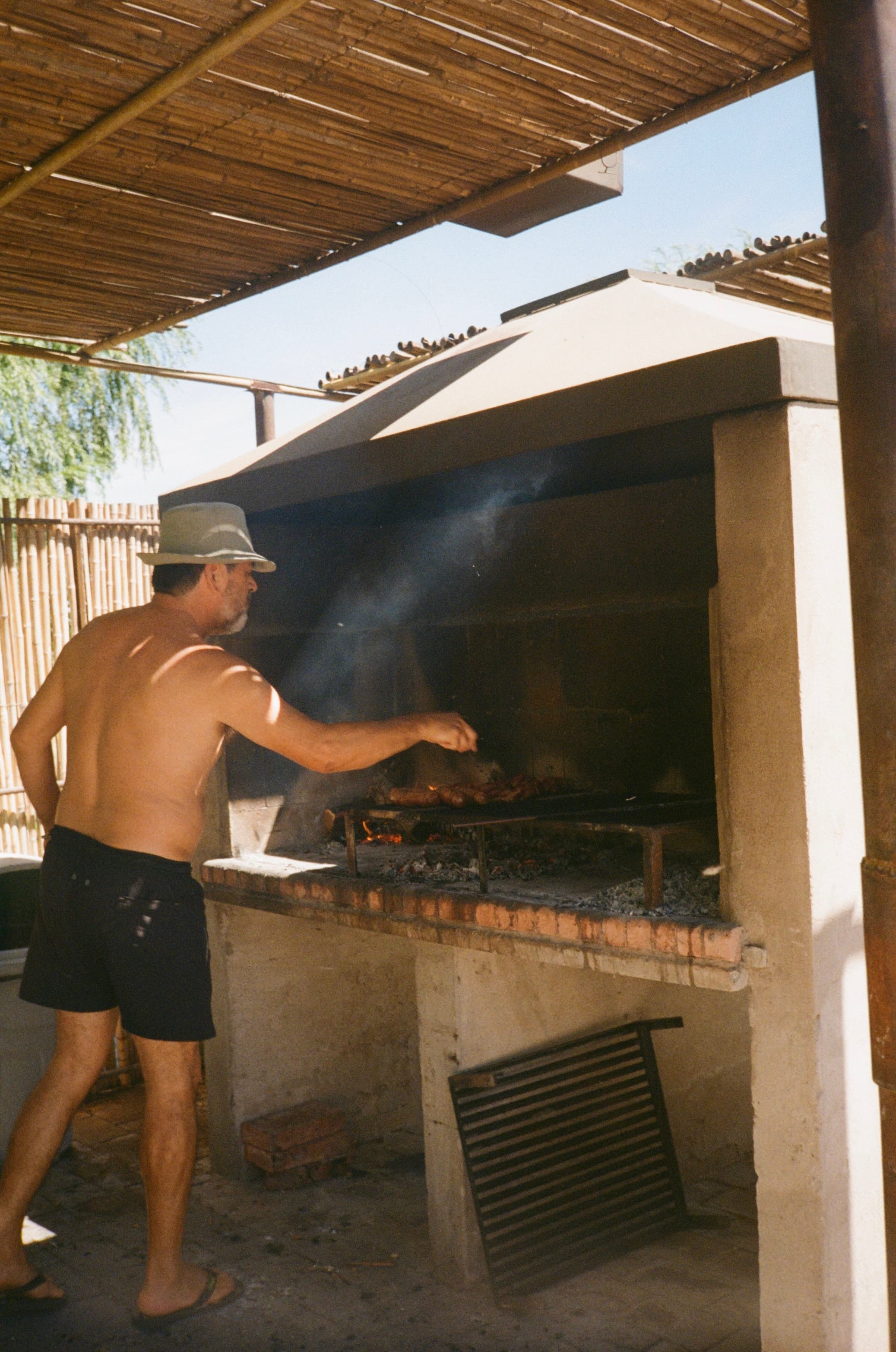 Un hombre atiende la parrilla bajo el techo de caña.