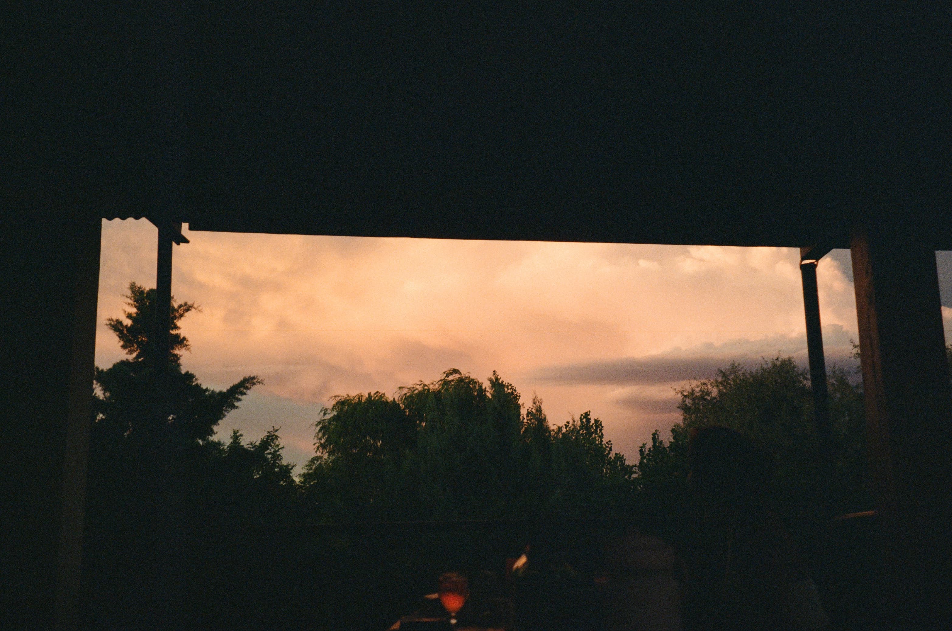El cielo del atardecer visto desde la terraza techada, con una copa sobre la mesa en penumbra.
