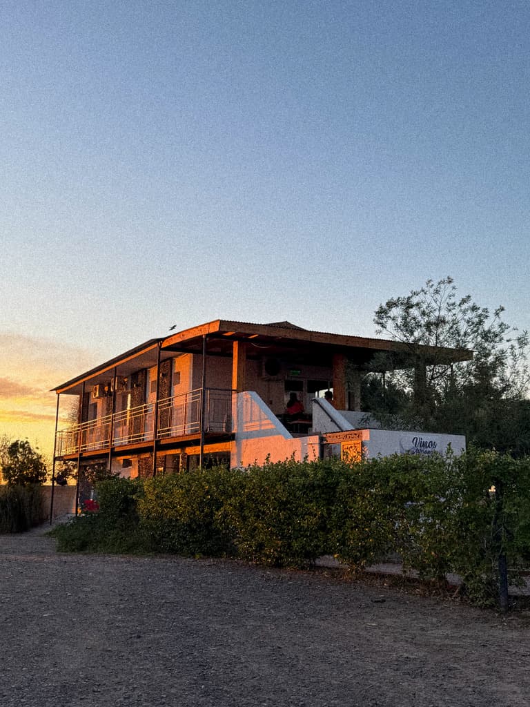 La casa de las habitaciones al atardecer, con la terraza de arriba y el cartel de Vinos sobre el muro.